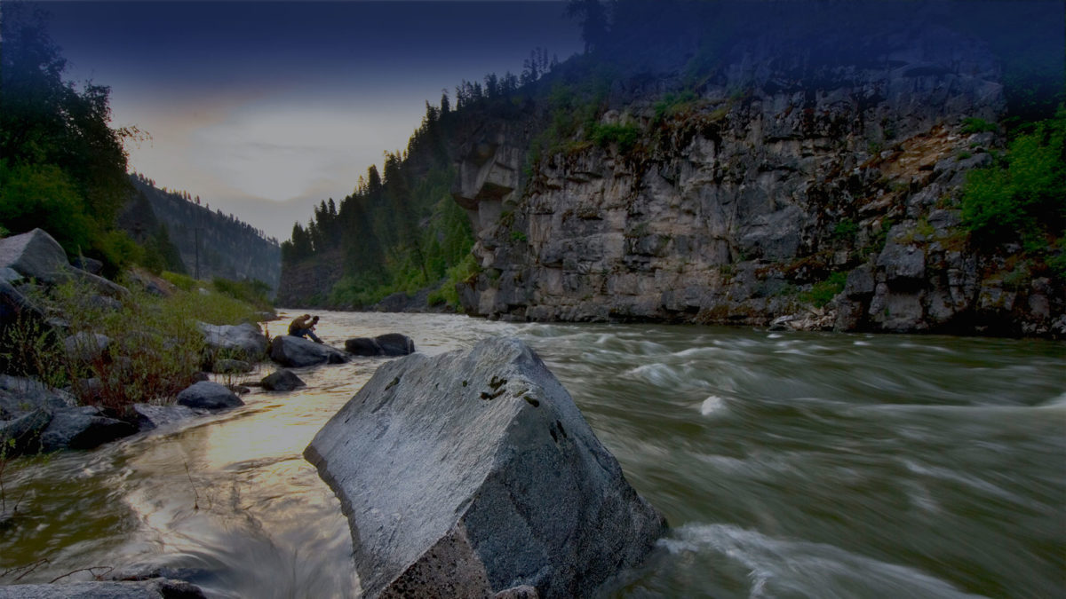 Sunrise reflecting off the fast-moving Payette River around a large Rock in the middle of the flow with a photographer in the distant background